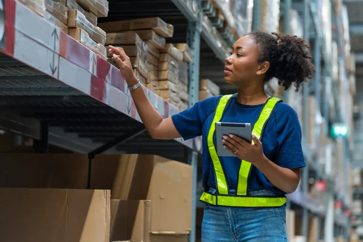 Warehouse worker scanning stock on a handheld device between shelves of boxes