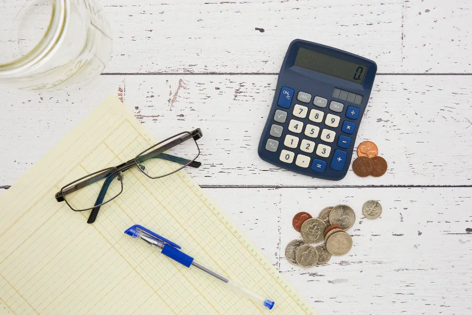 Calculator, coins, glasses and pen on a ledger pad