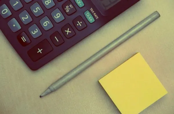 Calculator, pencil and yellow sticky note on a desk