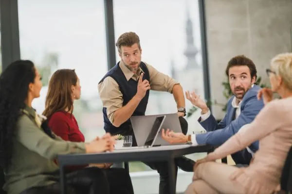 Colleagues debating around a meeting table with laptops