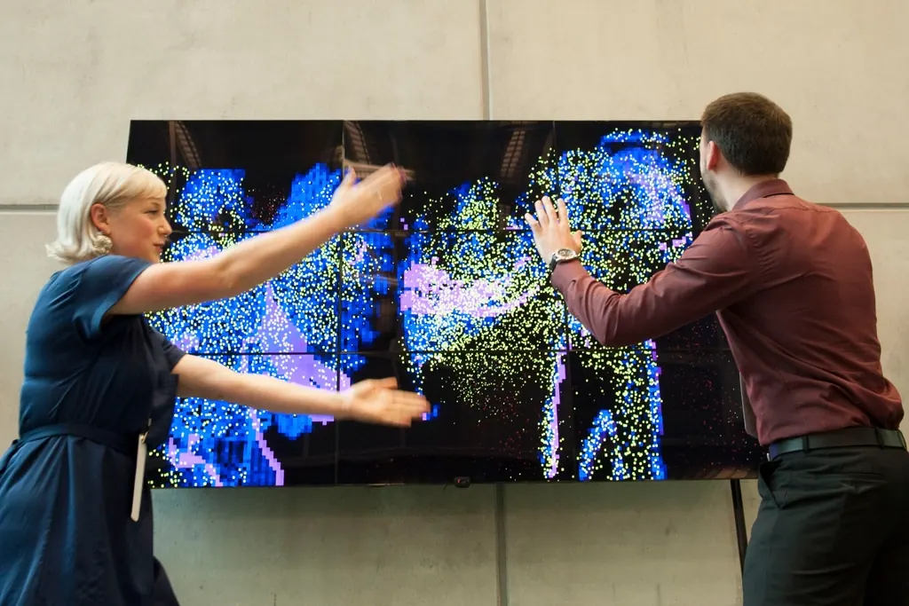 Two colleagues pointing at data on a large wall screen