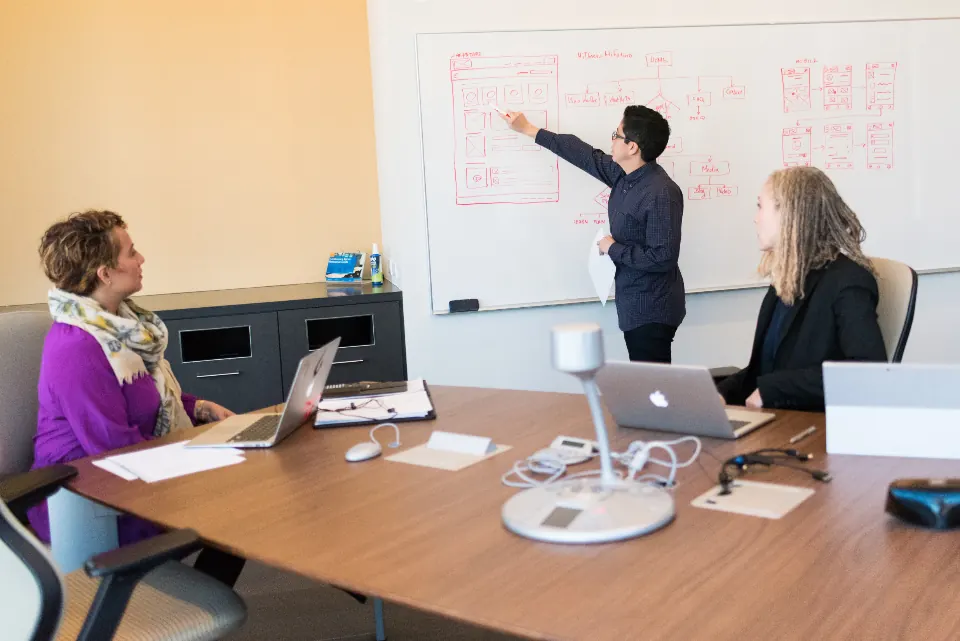 Consultant leading a workshop at a whiteboard with two colleagues