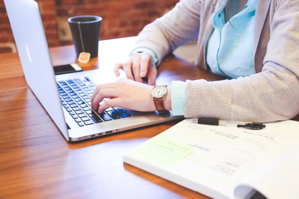 Coordinator typing order details on a laptop beside a notebook
