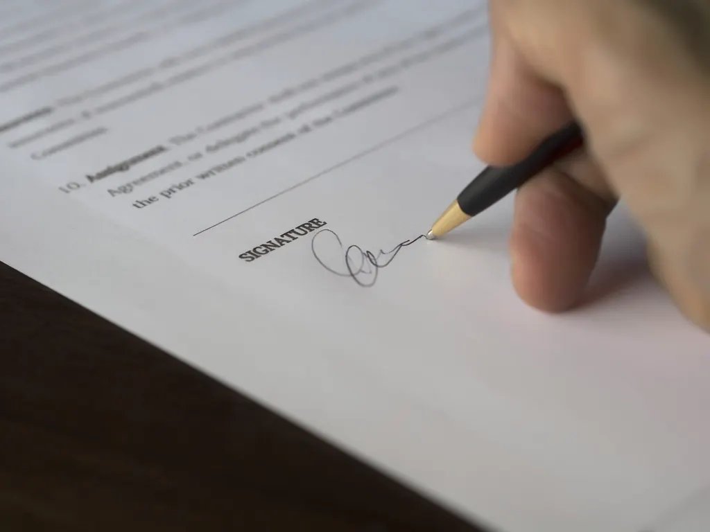 Finance director signing a printed project agreement at a desk