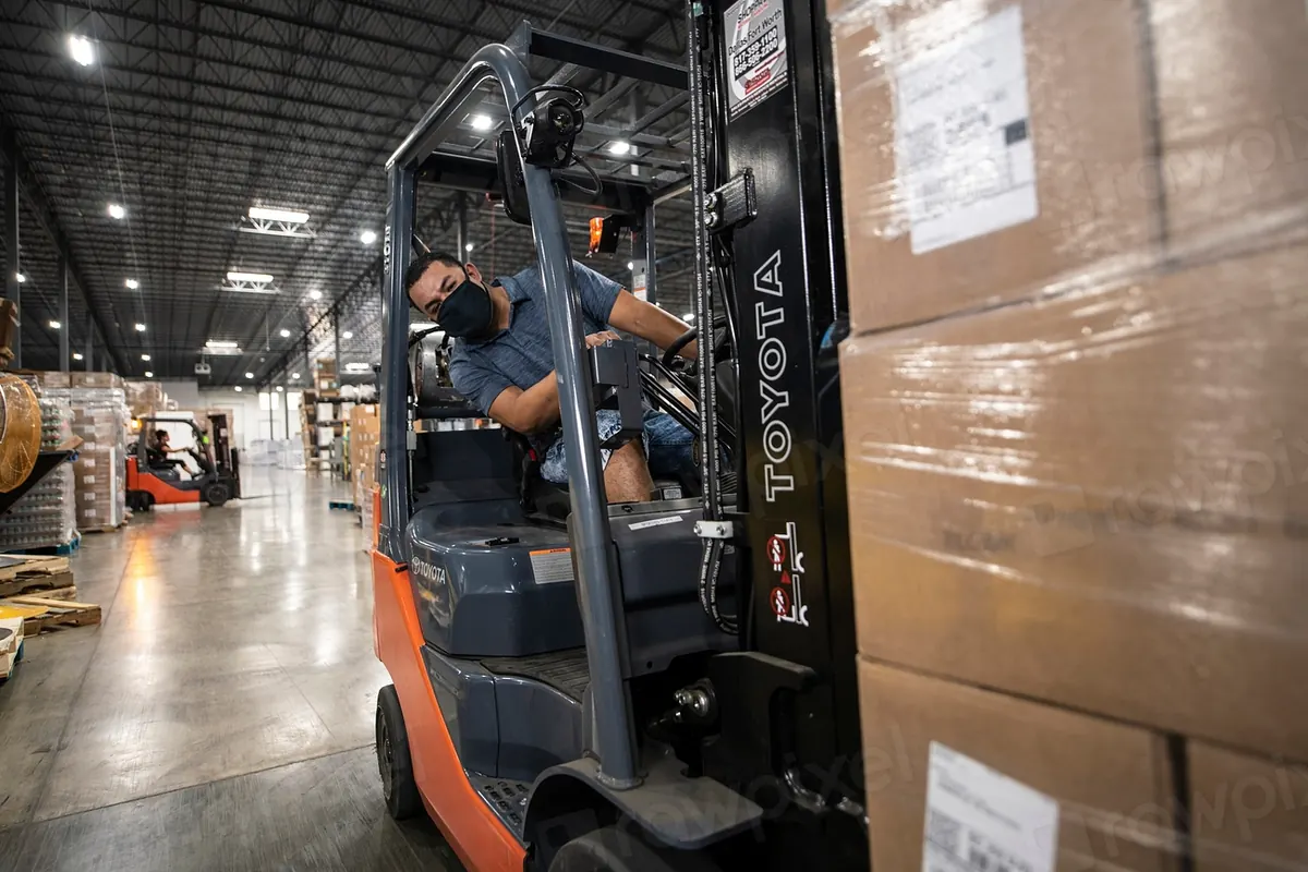 Forklift working an aisle of stacked cartons in a warehouse
