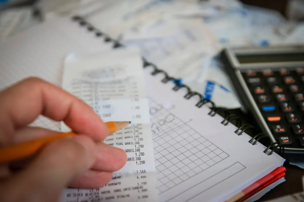 Hand checking printed figures with a pencil beside a calculator