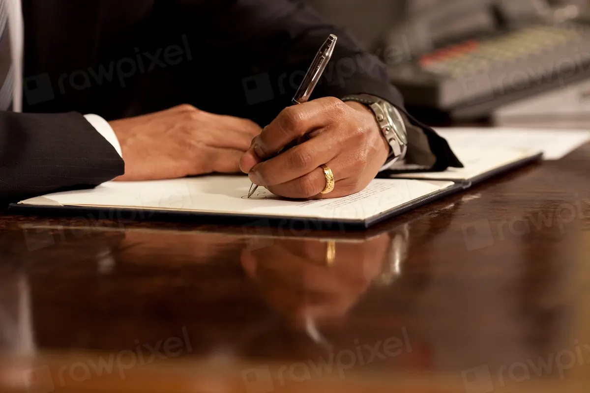 Hand signing a document with a pen at a desk