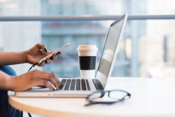 Hands on a laptop and phone beside a coffee cup
