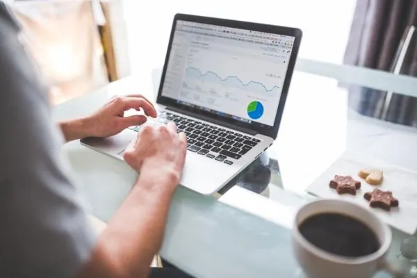 Hands on a laptop showing a pie chart and a spreadsheet