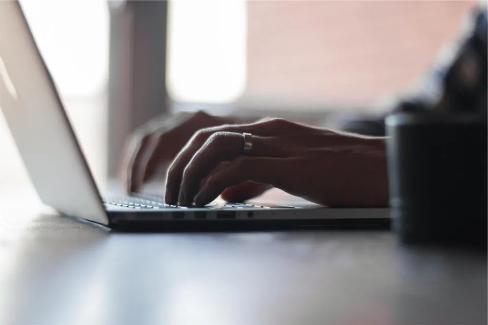 Hands typing on a laptop keyboard on a white desk