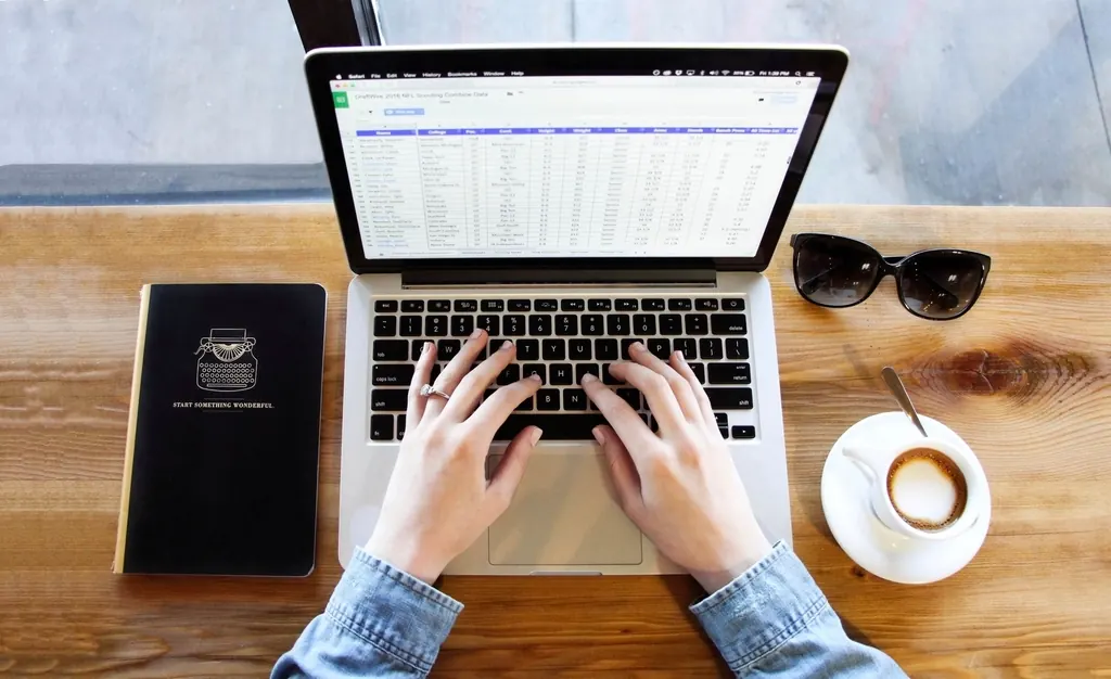 Hands typing on a laptop showing a spreadsheet, beside a coffee cup