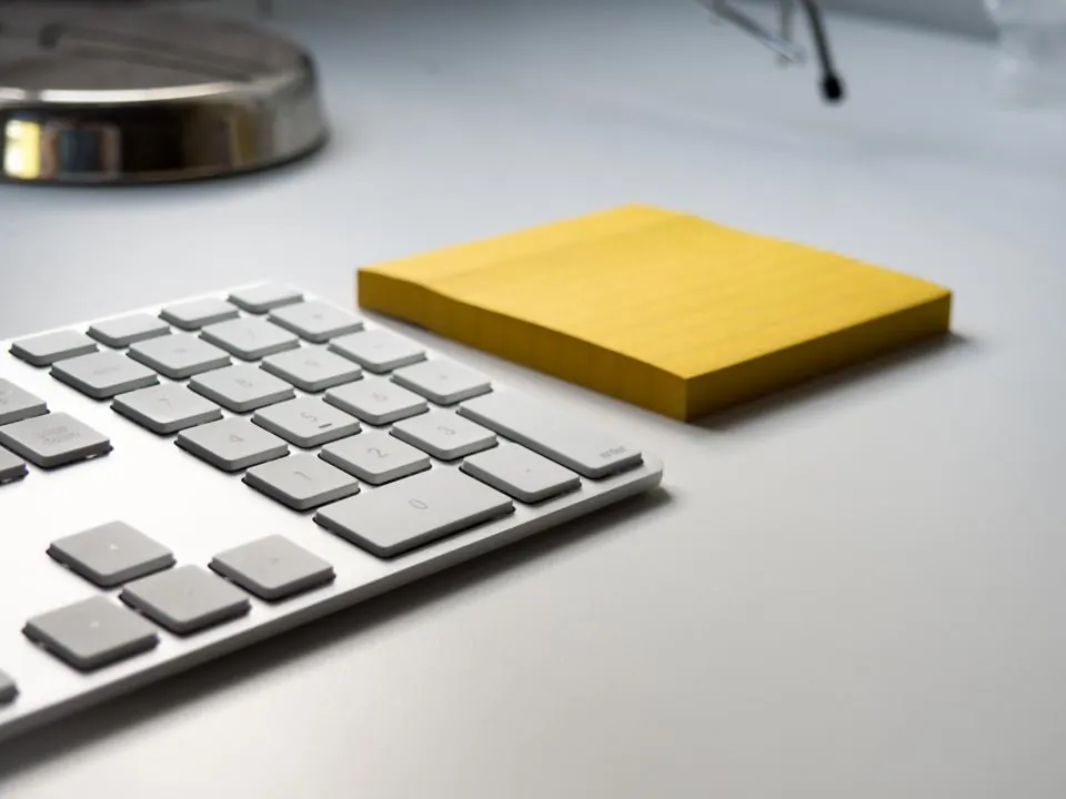 Keyboard and a yellow sticky note on a white desk