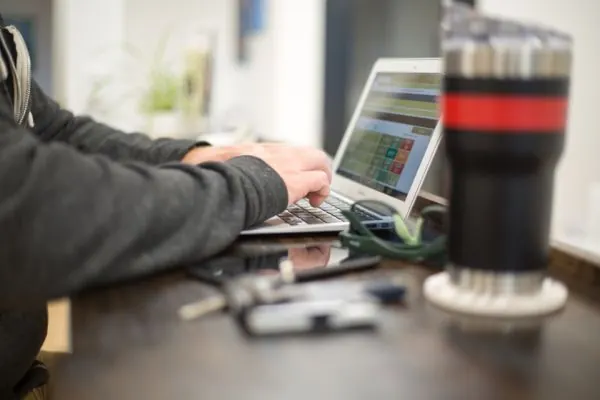 Man typing on a laptop beside a glass on a dark desk