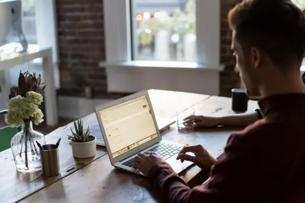 Man typing on a laptop at a desk by a window