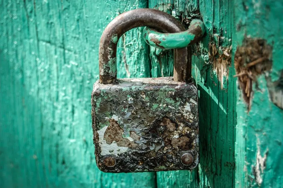 An old padlock hanging on a green painted door
