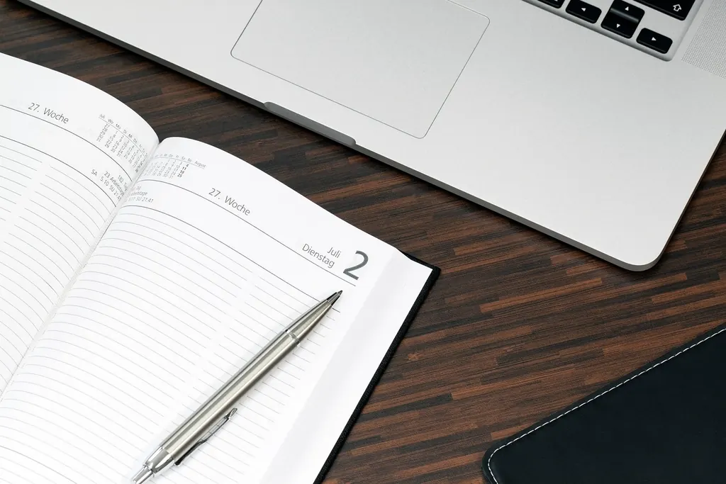 Open notebook and pen beside a laptop on a desk