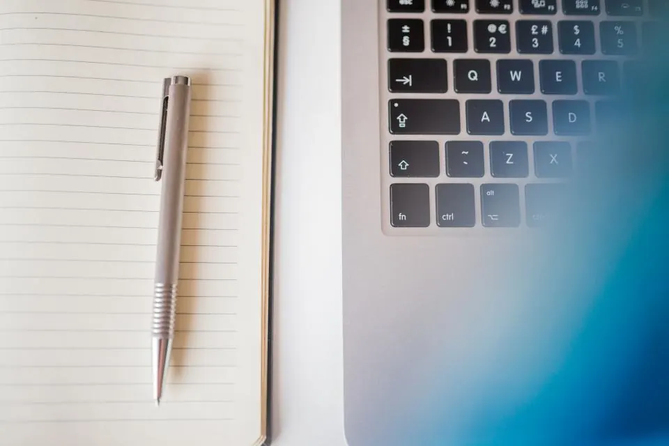 Open notebook and laptop on a wooden desk beside coffee