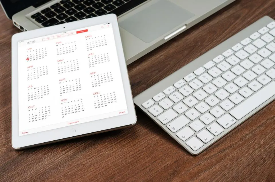 Tablet showing a calendar beside a keyboard on a wooden desk