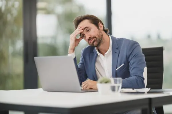 Tired man rubbing his forehead while working at a laptop