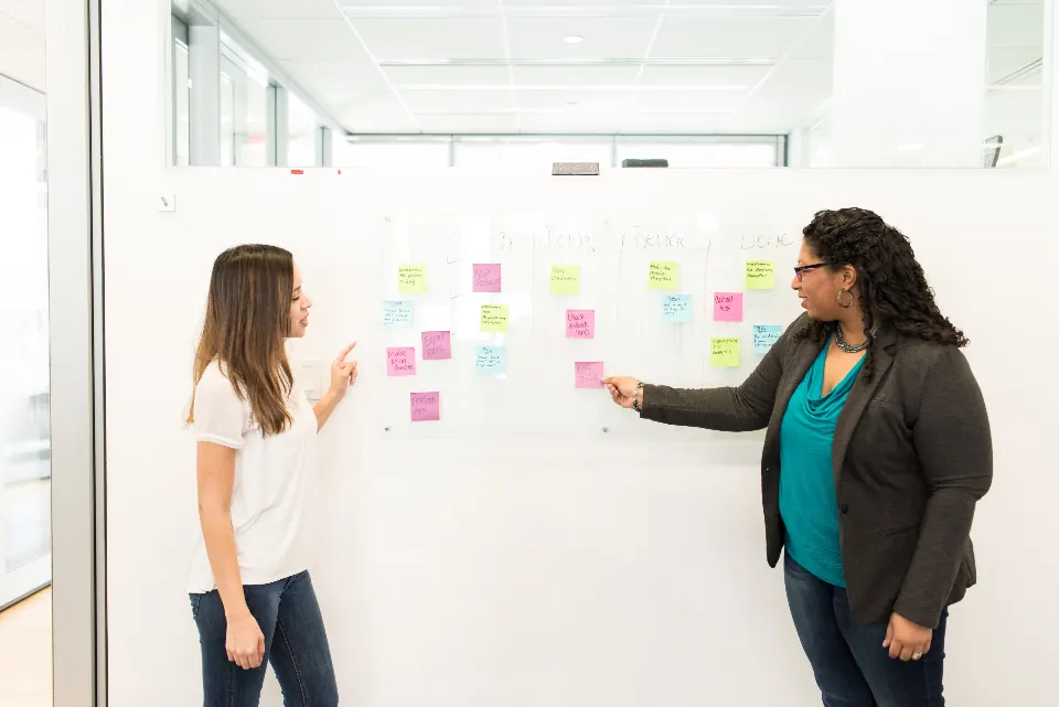 Two women mapping a process with sticky notes on a wall