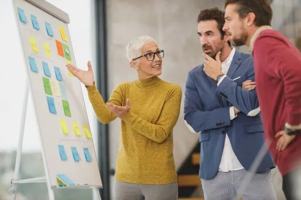 Woman presenting a sticky note board to two colleagues
