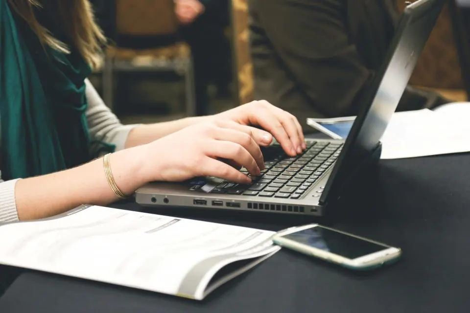 Woman typing on a laptop with her phone and papers beside it