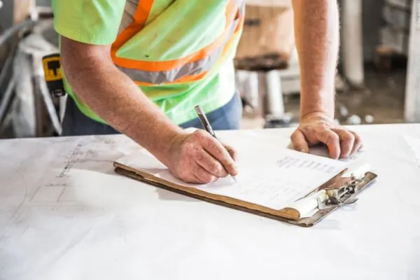 Worker in a safety vest writing on a clipboard