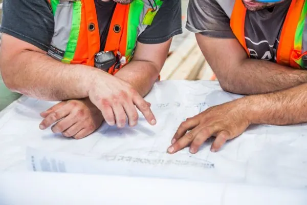 Workers in safety vests reading blueprints together